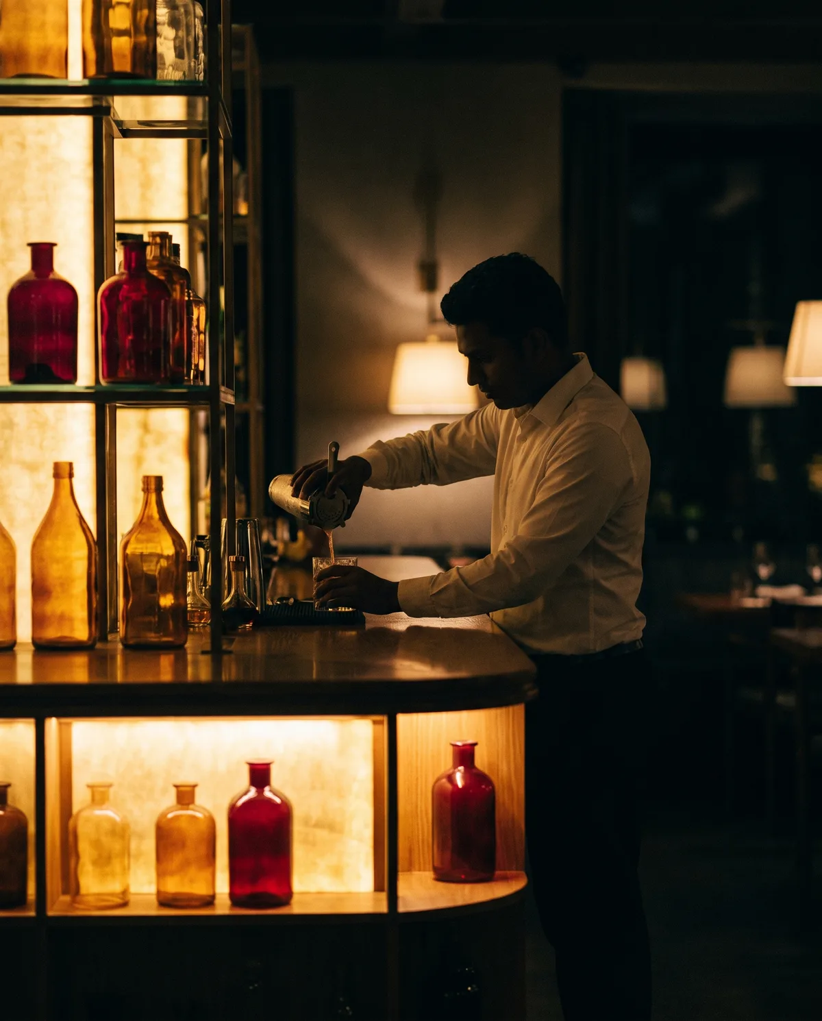 A bartender pouring a cocktail behind a backlit bar