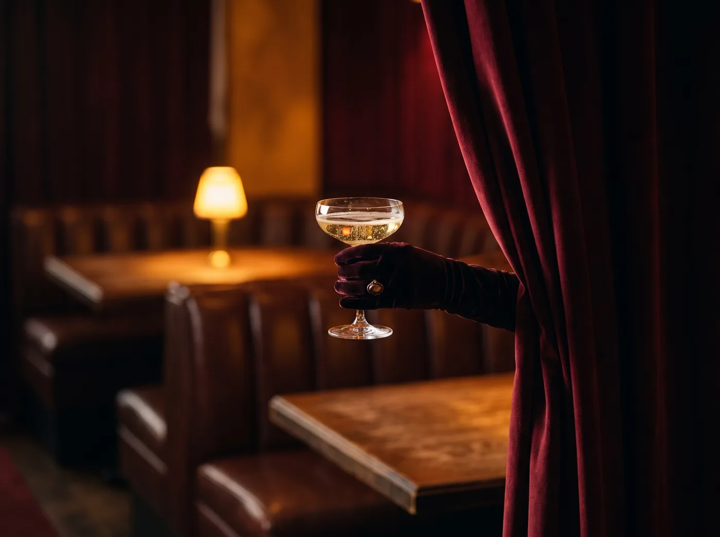 A hand holding a coupe of champagne beside a dark red curtain