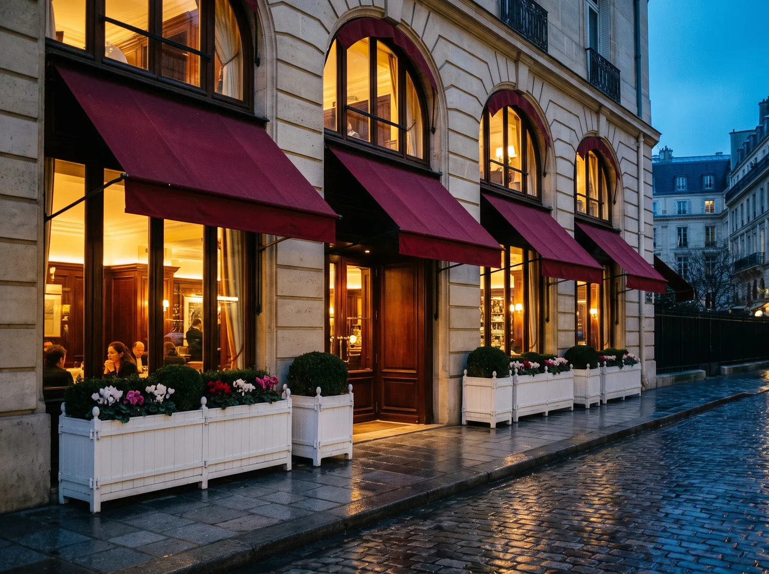 The Haussmann facade of L'Essence du Rouge at dusk with red awnings