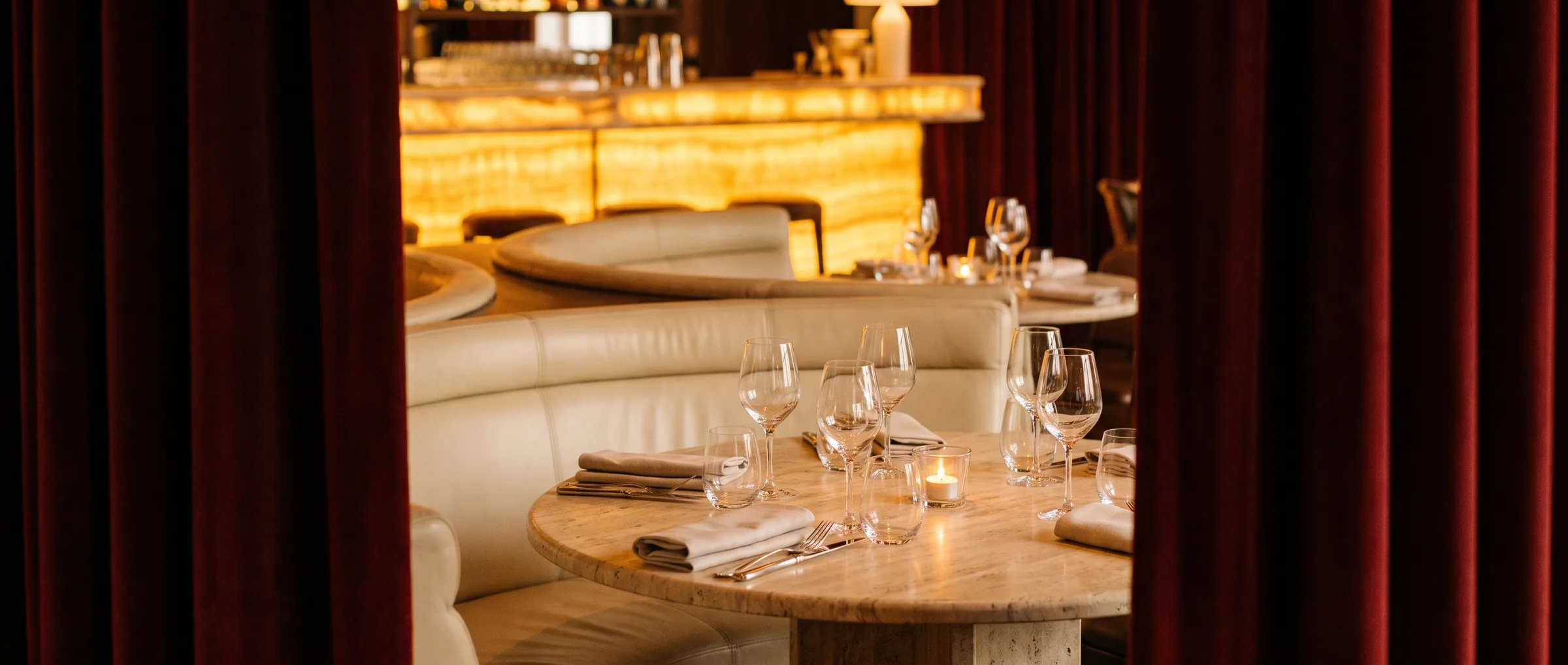 A table set for two between deep red velvet curtains in the dining room of L'Essence du Rouge