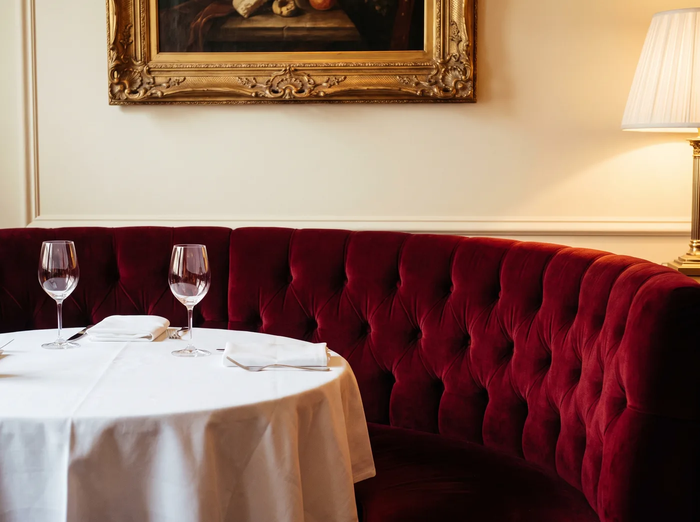 A crimson velvet banquette behind a table set with white linen